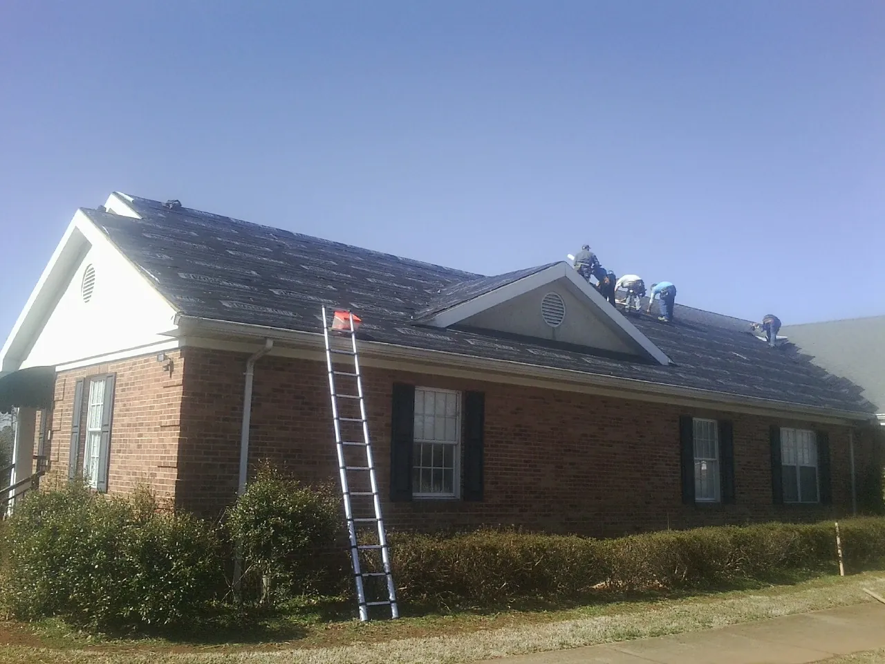 Crew tearing shingles off a brick ranch roof with a ladder set — Metal Roof Repair work by our crew in Whitman