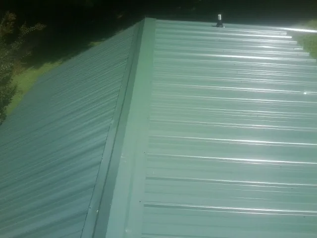 New green metal panels meeting at the ridge of a roof — Flat Roof Repair work by our crew in Whitman