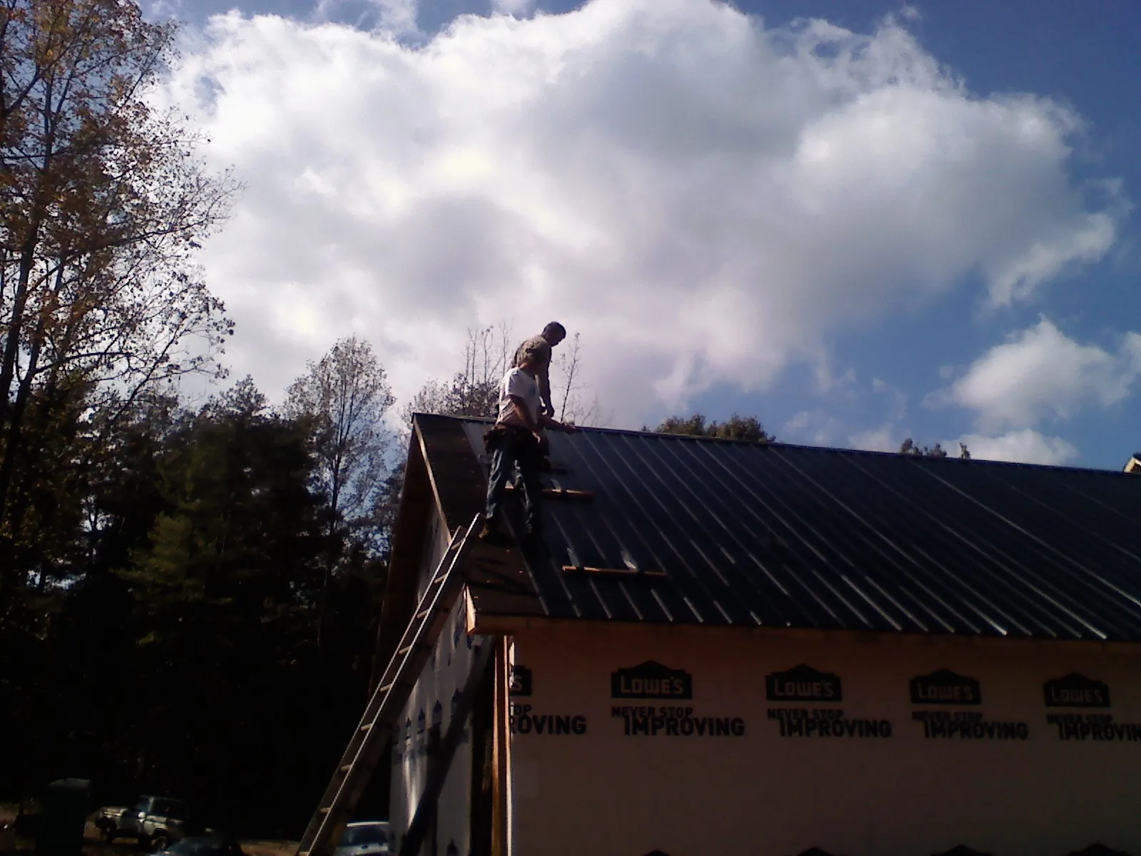Roofer fastening dark metal panels high against a cloudy sky, from a Roof Inspection job in Whitman