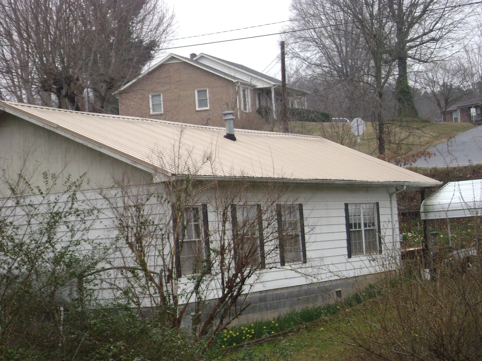 Tan metal roof on a white sided house set into a hillside — Commercial Roofing by Roofing Brothers in Whitman